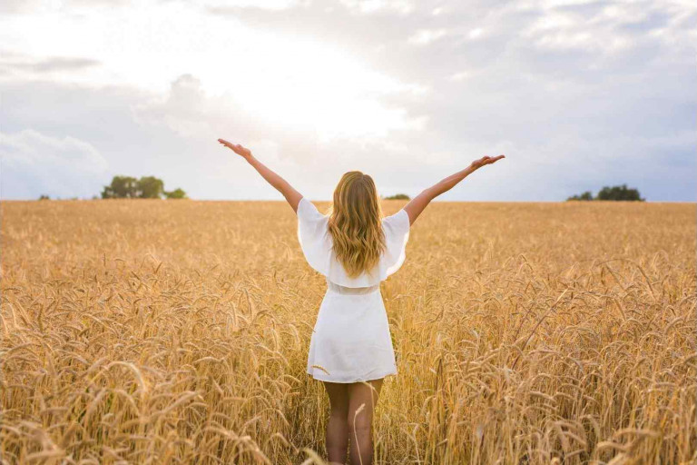 femme de dos les bras en l'air dans un champs de blé